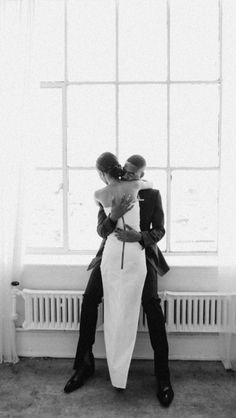 a man and woman sitting on a window sill with their arms around each other