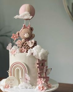 a white cake with pink decorations and a teddy bear on top