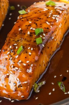 salmon with sesame seeds and green onions in a brown sauce on a black plate, ready to be eaten