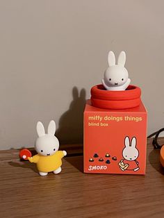 two small plastic rabbits sitting on top of a wooden table next to a red box