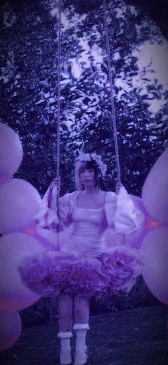 a woman in a dress sitting on a swing with balloons attached to her legs and feet