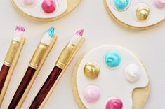 three decorated cookies with paintbrushes and brushes next to them on a white surface