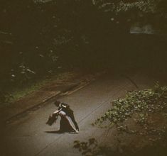 two people are dancing on the sidewalk in the dark with their arms around each other