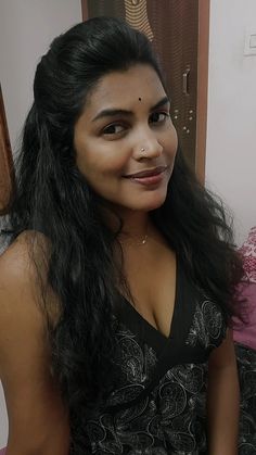 a woman with long black hair is smiling for the camera while sitting on a bed