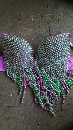 a purple and green beaded bralet laying on the ground next to a pair of scissors