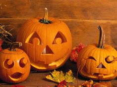 three carved pumpkins sitting next to each other on a wooden surface with autumn leaves around them