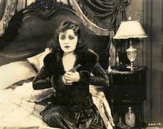 an old black and white photo of a woman sitting on a bed looking at her cell phone