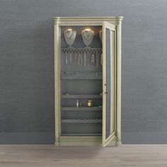 an open cabinet with necklaces and jewelry in it on a wooden floor next to a gray wall