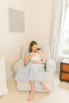 a woman sitting in a chair holding a baby while wearing a blue and white dress