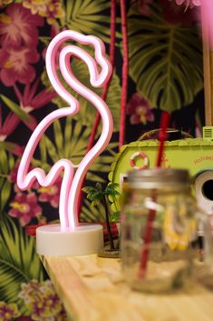 a pink flamingo neon sign sitting on top of a wooden table next to a jar