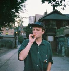 a young man standing on the sidewalk talking on a cell phone while wearing a hat