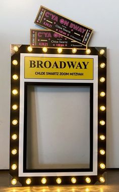 the broadway sign is lit up in front of a white wall with yellow and black lights