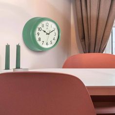 a clock on the wall above a table in a room with pink chairs and curtains