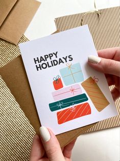 a hand holding a card with the words happy holidays written on it and presents wrapped in brown paper