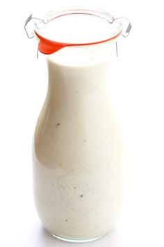 a glass bottle filled with milk sitting on top of a white table next to a red handled spoon