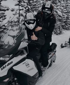 two people on snowmobiles with trees in the background