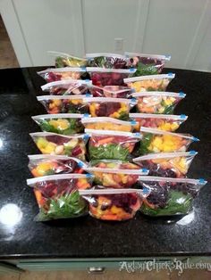 plastic bags filled with fruit sitting on top of a black counter next to a refrigerator