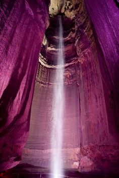 the light is shining brightly in this cave with pink walls and purple fabric draped around it