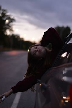 a young woman leaning out the window of a car at night with her hand on the door handle