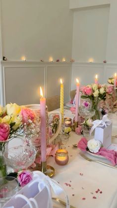 the table is set with pink and yellow flowers, candles, and napkins on it