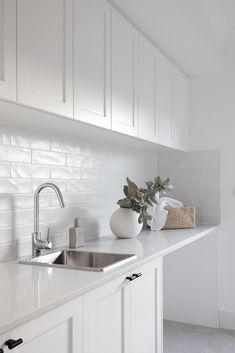 a kitchen with white cabinets and countertops has a sink, faucet, soap dispenser and towel rack