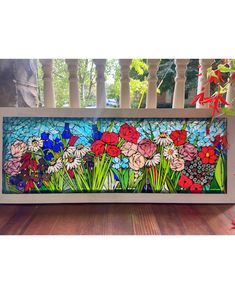 a stained glass window sitting on top of a wooden bench next to flowers and plants