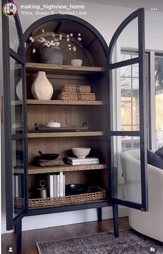 an open bookcase in the corner of a living room filled with books and vases