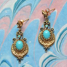 A gorgeous pair of ornate dangle earrings fashioned in 14 karat yellow gold, each set with turquoise cabochons. The turquoise is a bright and vivid slightly greenish blue, one oval and one round per earring. A golden post with ornate detailing balances above a second, decorative dangle element. The round turquoise cabochon is prong set above a textured crescent shaped element, within which the oval cabochon is bezel set with an ornate golden textured bezel. These post style earrings come complete with a pair of 14k gold friction backs. More details: 37.2mm total length, 14.1mm width, largest turquoise cabochons measure 6.0mm wide and 8.0mm tall. Excellent condition 14k (stamped) 6.3 grams All purchases arrive in a gift box, wrapped with a ribbon. Golden Texture, Greenish Blue, Vintage Turquoise, Style Earrings, Oval Cabochon, Jewelry Earrings Studs, Prong Setting, Fashion Earrings, Favorite Jewelry