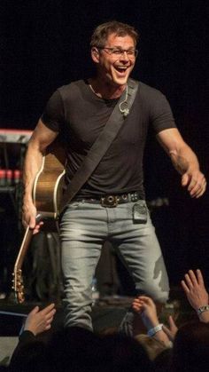 a man standing on top of a stage holding a guitar and singing to an audience