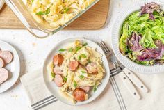 two plates of food on a table next to a bowl of pasta and a plate of salad