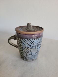 a ceramic cup with a lid and handle sitting on a white tablecloth covered surface