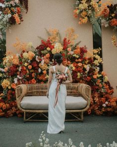 a woman standing in front of a flower display with flowers on the wall behind her