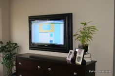 a television mounted on the wall above a dresser with books and plants in front of it