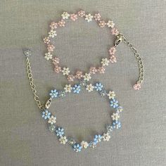 two bracelets with blue and pink flowers are on a gray tablecloth next to each other