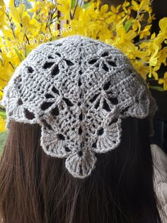 the back of a woman's head wearing a crocheted hat with flowers in the background