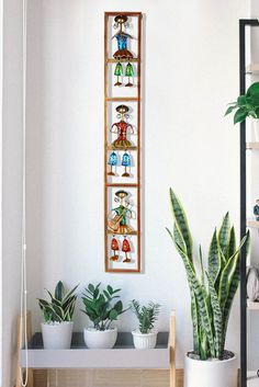 a room with some plants and pictures on the wall above it in front of a shelf