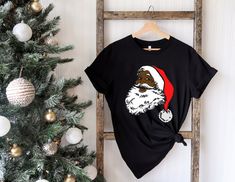 "Black Santa Claus Shirt, Black Santa Claus Tee, African American Christmas Tee, African American Santa Shirt, Christmas Tee, Xmas Gift Shirt ⭐Please Check All Photos For Details.   🐞Choose Your T-Shirt Size From The Drop-Down Lists Next To The item Picture   ⭐Choose Of Your T-Shirt Color From The 2nd Picture   🐞Use \"Add message to Seller\" link On The Checkout Page To Send me the Following important Details For Your Order's Customization.   ⭐Shipping Time Varies by location (we are located in Sugar Land, Texas) please consider that our turn around time is 1 to 3 business days.     ⭐Which brand do you use for t-shirts? We use Gildan, Bella Canvas Unisex, Hanes, District, Outlash and Next Level when we have a shortage of stocks for certain colors and sizes. Our printing method is premium Black Santa Tee Dress, Black Christmas T-shirt As Gift, Black Christmas Graphic Tee, Black Crew Neck Christmas T-shirt, Black Santa Shirt, Black Santa Claus, African American Christmas, American Christmas, Santa Shirt