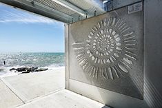 an artistic metal artwork on the side of a building next to the ocean and beach