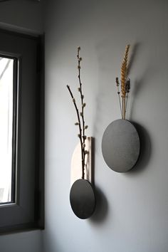 two round metal vases on the wall next to each other with flowers in them