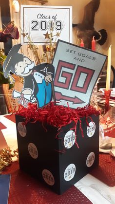 a black box with red ribbon and some cards in it sitting on a table next to candles