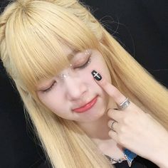 a woman with long blonde hair and black eyeliners holding her finger up to her nose