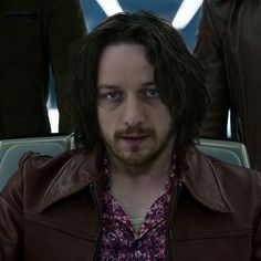 a man with long hair wearing a brown leather jacket in front of two other men