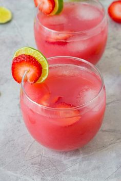 two glasses filled with pink lemonade and strawberries next to lime slices on the rim