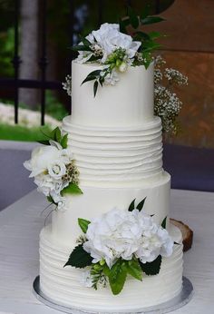 a three tiered white wedding cake with flowers on the top and bottom, sitting on a table