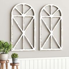 two white arched window frames on the wall next to potted plants and stools