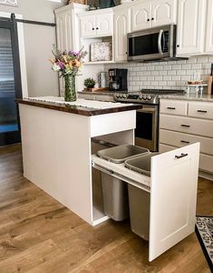 a kitchen with white cabinets and an island that has trash cans in the bottom drawer