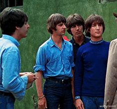 the beatles standing in front of a green wall with their heads turned to one side