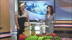 two women standing in front of a table with food on it and a tv screen behind them