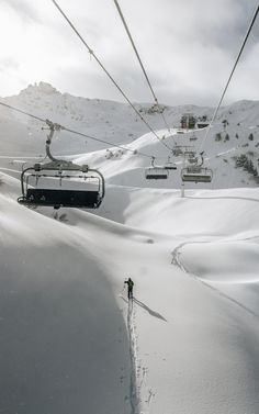 a ski lift going up the side of a snow covered mountain next to a person