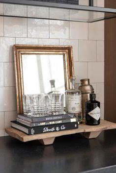 a shelf with books and glasses on top of it next to a framed mirror in a kitchen